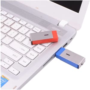 A red and blue Ginan Swivel Flash Drive plugged into a laptop USB port, positioned on a silver laptop keyboard.