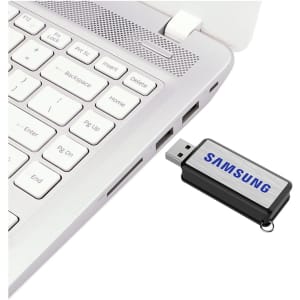 A black and silver flash drive is connected to a laptop's USB port, featuring a logo.