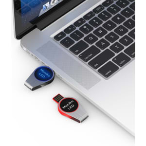 A red and black Monika LED flash drive is plugged into a laptop, showcasing its sleek design and branding.