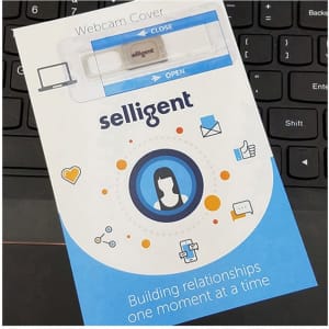 A webcam cover in a white and blue packaging, with a logo, placed on a black keyboard.