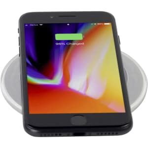 A black smartphone displaying a charged battery on a round, clear wireless charging pad. The pad has a subtle design.