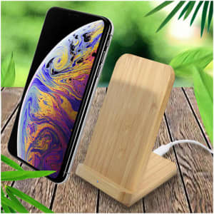 A wooden bamboo wireless charger stands upright beside a smartphone, set against a leafy background.