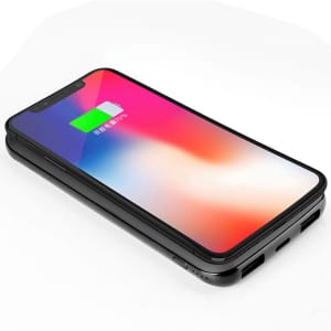 A black wireless power bank with a smartphone on top, displaying a charging indication on the screen.