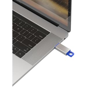 A silver and blue flash drive is plugged into a laptop's USB port, with the laptop keyboard visible in the background.