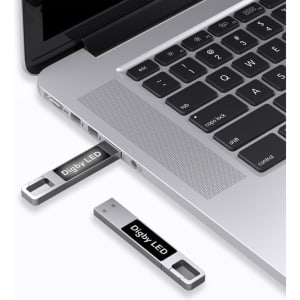 A silver LED flash drive connected to a laptop's USB port, featuring a logo on the drive.