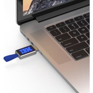 A silver LED flash drive with a blue pull tab is plugged into a laptop's USB port.