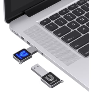 A compact black LED flash drive connected to a silver laptop, featuring a logo on the drive.