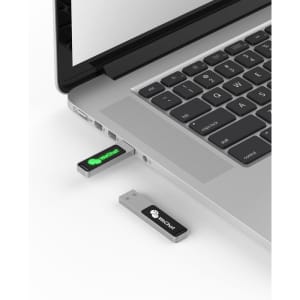 A USB flash drive in silver and black, partially inserted into a laptop's USB port, with branding visible.