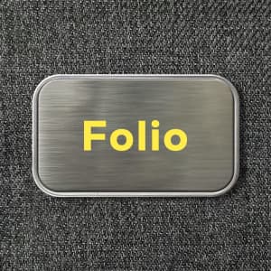 A metallic rectangular container with a brushed finish and a yellow logo. The background is a textured dark fabric.