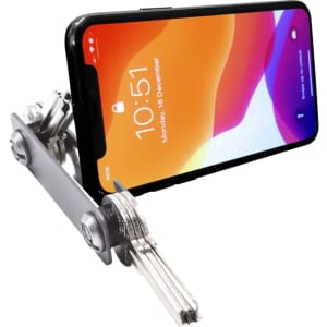 A silver keyring device holds a smartphone at an angle, showcasing its screen. The phone displays a colourful wallpaper.