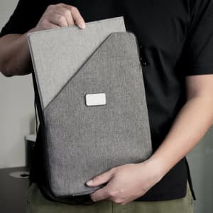 A grey foldable mouse pad is being held, featuring a textured surface and a logo. It's sleek and portable in design.