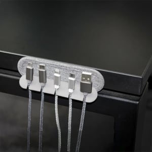 A cable organiser in grey holds multiple charging cables against a black surface. It features a fabric-like texture and a sleek design.