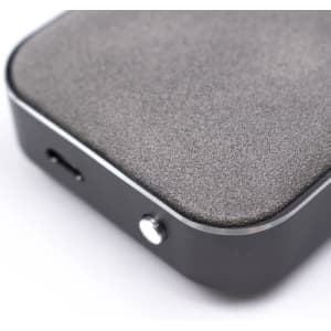 A Bluetooth speaker with a matte grey surface and a shiny black edge, featuring a charging port and a button.