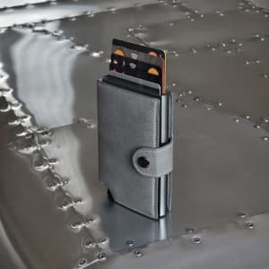 A grey vegan wallet stands upright on a metallic surface, displaying multiple cards partially visible from its opening.