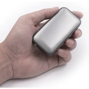 A compact silver wireless speaker held in a hand, featuring a perforated design and a sleek shape.