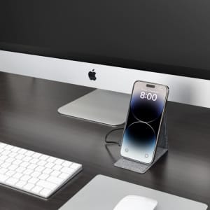 A wireless charger in dark grey, holding a smartphone, placed on a desk beside a computer and keyboard.