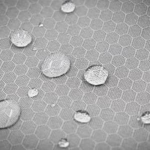A close-up of a textured grey fabric with water droplets collecting on its honeycomb pattern, featuring a logo.