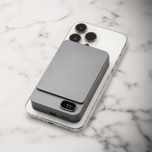 A grey magnetic wireless power bank rests on a smartphone, displaying a sleek and modern design against a marble background.