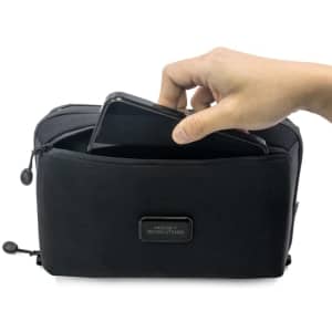 A black toiletry bag with a hand placing a phone inside, featuring a logo on the front.