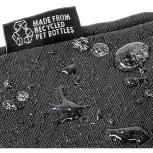 A close-up of a black toiletry bag with a textured surface and water droplets, featuring a small tag.