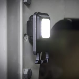 A black multi-tool with a COB LED light attached to a metal surface, featuring a compact design and a functional clip.