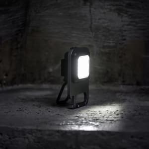 A compact black multi-tool LED light positioned on a textured surface, with a bright light emanating from its front.