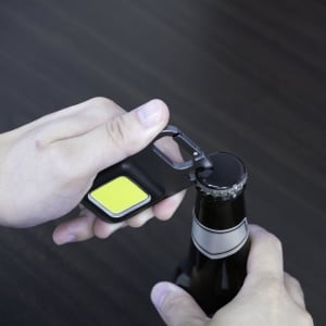 A multi-tool bottle opener with a black body and yellow grip, being used to open a bottle.