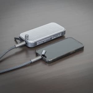 A silver Bluetooth speaker power bank connects to a black smartphone, resting on a wooden surface.