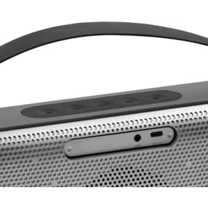 A wireless speaker in grey with a sleek design, featuring control buttons and a logo on the front.