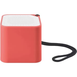 A compact square speaker in coral with a textured white top and a black strap attached.