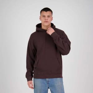 A model wearing a brown hoodie with a front pocket and a logo, paired with blue jeans.