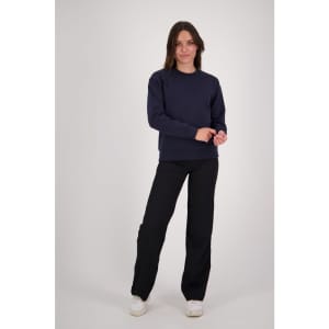 A woman stands confidently in a navy crew neck sweatshirt and black pants, with a logo visible on the sweatshirt.