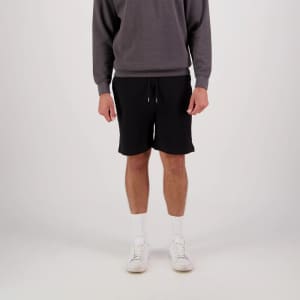 Black sports shorts with a drawstring waist, modelled with a grey sweatshirt and white socks and shoes. Features a logo.