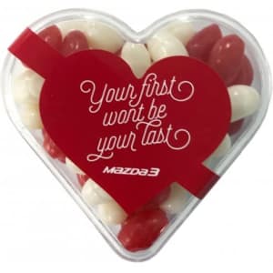 Acrylic heart-shaped container filled with red and white mini jelly beans, featuring a logo and festive design.