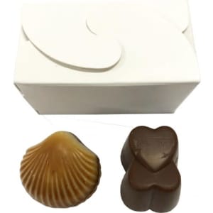 A white box contains two chocolates: a brown heart-shaped piece and a caramel sea shell-shaped chocolate.