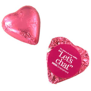 A pink chocolate heart wrapped in shiny foil, accompanied by a decorative foil wrapper with a logo.