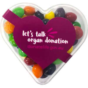 A heart-shaped acrylic container filled with colourful Skittles sweets, featuring a purple label.
