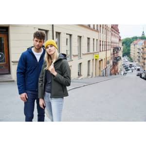 A navy and olive green softshell jacket worn by a man and woman on a city street. The woman also wears a yellow beanie.