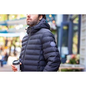 A man wearing a black puffer jacket, holding a coffee cup, with a logo on the jacket sleeve.