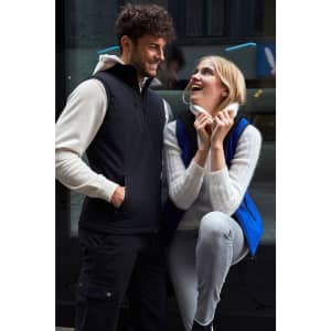 A black softshell vest worn by a man, paired with a blue softshell vest worn by a woman, both smiling.