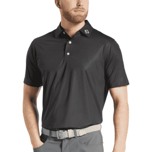 A black polo shirt with a collar and short sleeves, featuring a logo on the neckline. The model wears grey trousers.