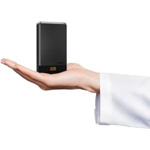 A hand holding a compact black power bank with a digital display and branding on one side.