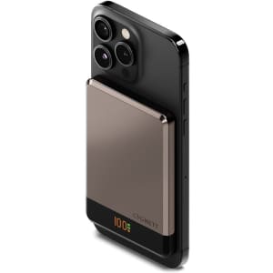 A slim, magnetic wireless power bank in grey is attached to the back of a black smartphone. It features a logo.