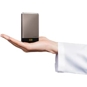 A compact silver and black wireless power bank held in a hand, featuring a small display.