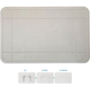A grey bath mat with a textured surface, featuring a logo. It has bordered sections and shows footprints.