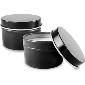 Two black tin candles with circular lids, one slightly open to reveal the wax inside.