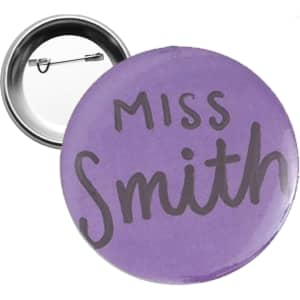 A round 58mm button badge in purple with a silver backing and a pin mechanism.