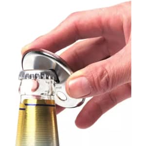 A drink bottle opener featuring a shiny silver magnet with a button badge design is being used to open a bottle.