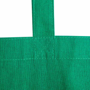 A close-up view of a green calico tote bag with stitched straps and no gusset. Features a logo.