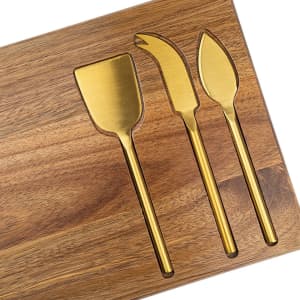 A wooden cheeseboard featuring three gold-coloured knives shaped for cutting and serving cheese.